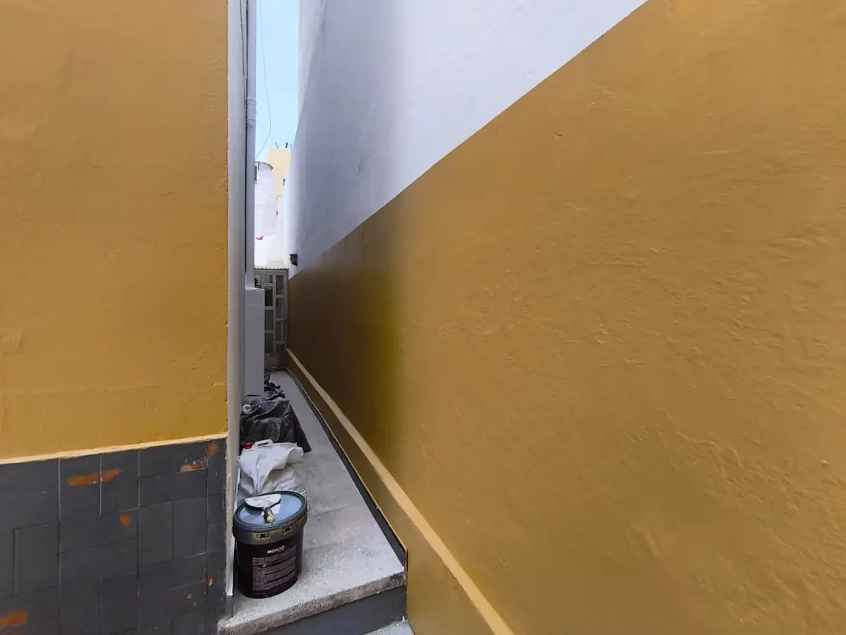 Pasaje lateral estrecho pintado en ocre y blanco tras la reforma
